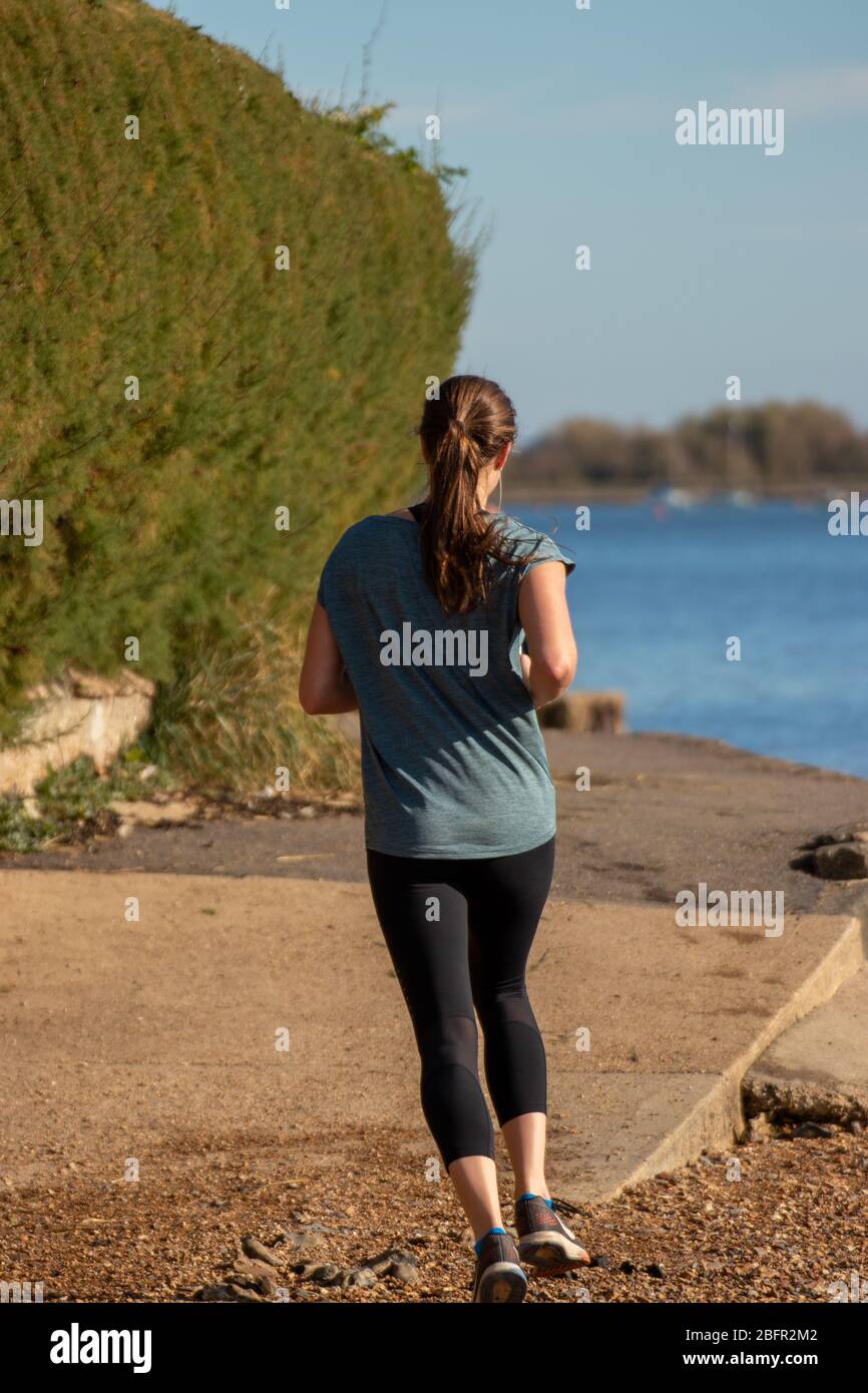 Una giovane donna che si fa jogging da sola lungo il lato della riva Foto Stock