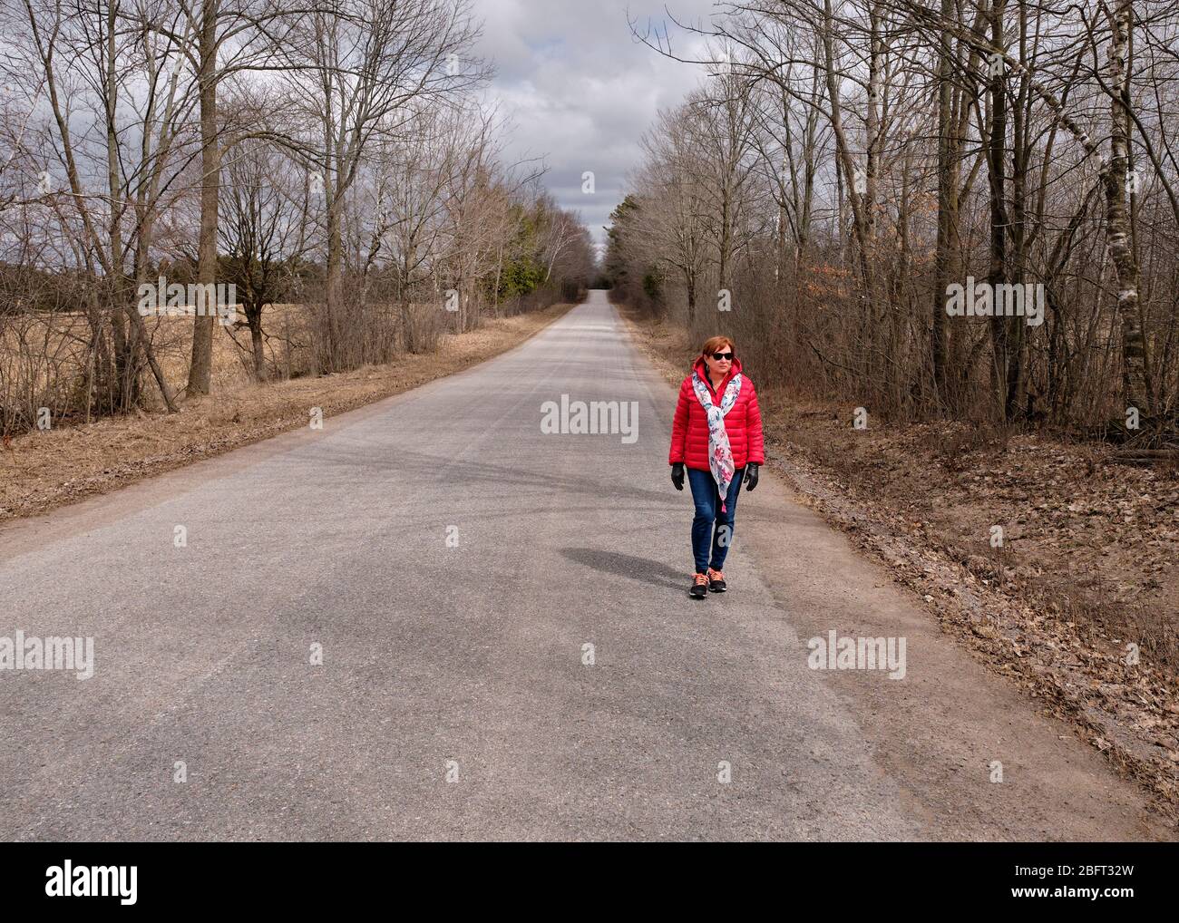 Una donna che indossa un cappotto rosso brillante cammina da sola lungo una strada di campagna durante la pandemia Covid-19. Foto Stock