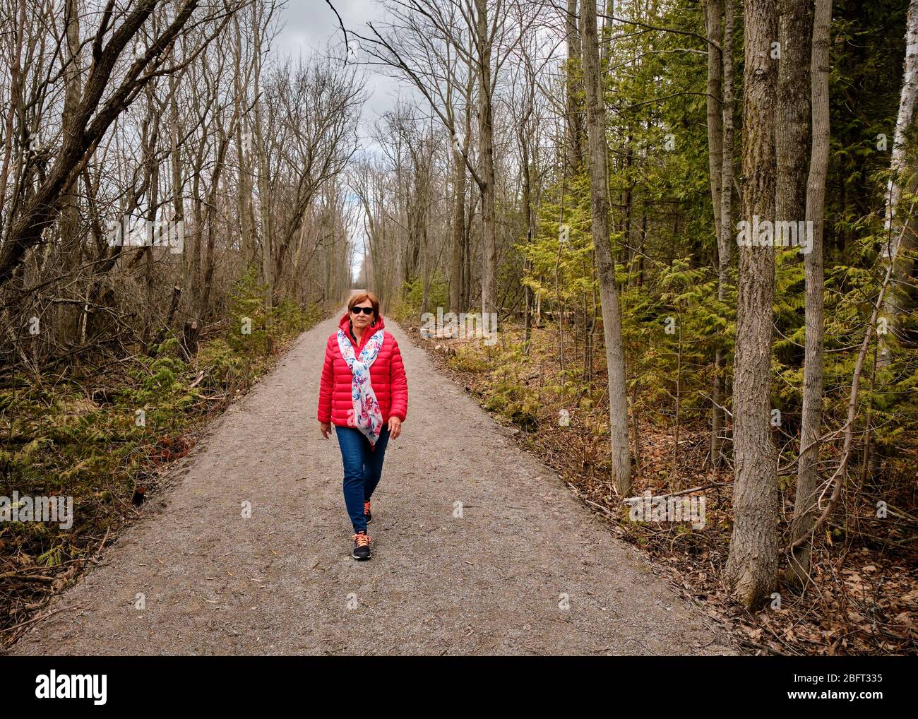 Una donna che indossa un cappotto rosso brillante cammina da sola lungo un sentiero forestale durante la pandemia Covid-19. Foto Stock