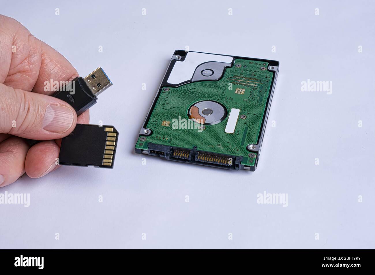 La mano contiene una chiavetta USB e una scheda SD, rispetto al disco rigido Foto Stock
