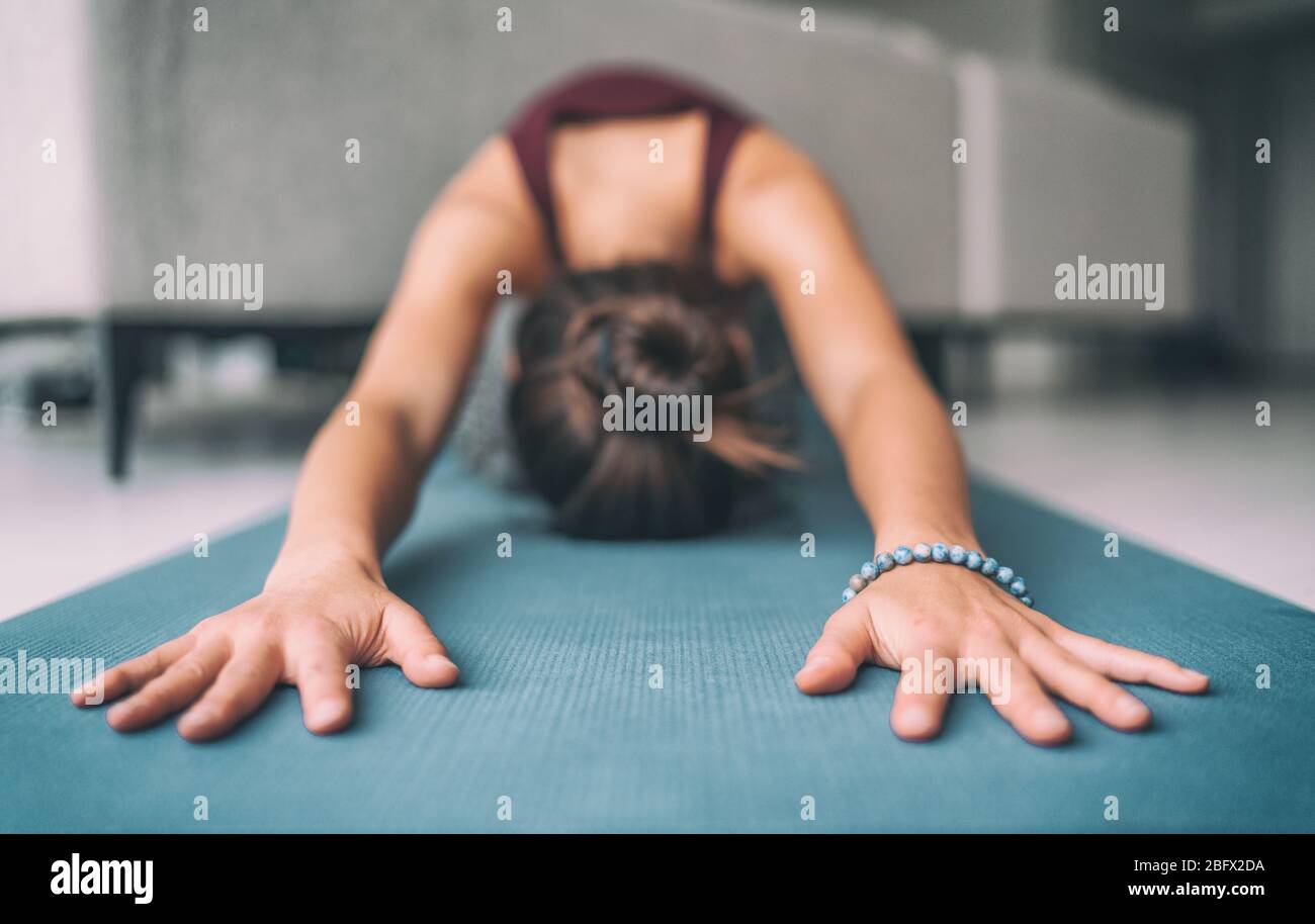 Yoga casa stretching meditazione donna facendo bambini posa riscaldamento stretch in soggiorno casa. Tappetino da ginnastica a contatto con le mani e bracciale mala. Fitness relax concetto senza stress. Foto Stock