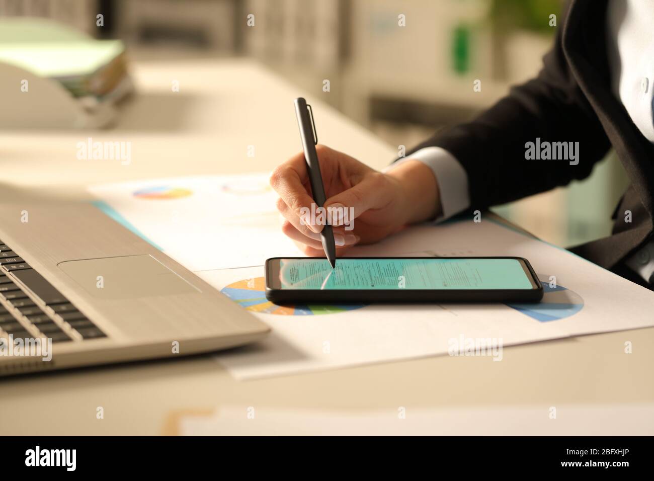 Primo piano delle mani di una donna executive compilando il modulo con lo stilo sullo smartphone di notte in ufficio Foto Stock