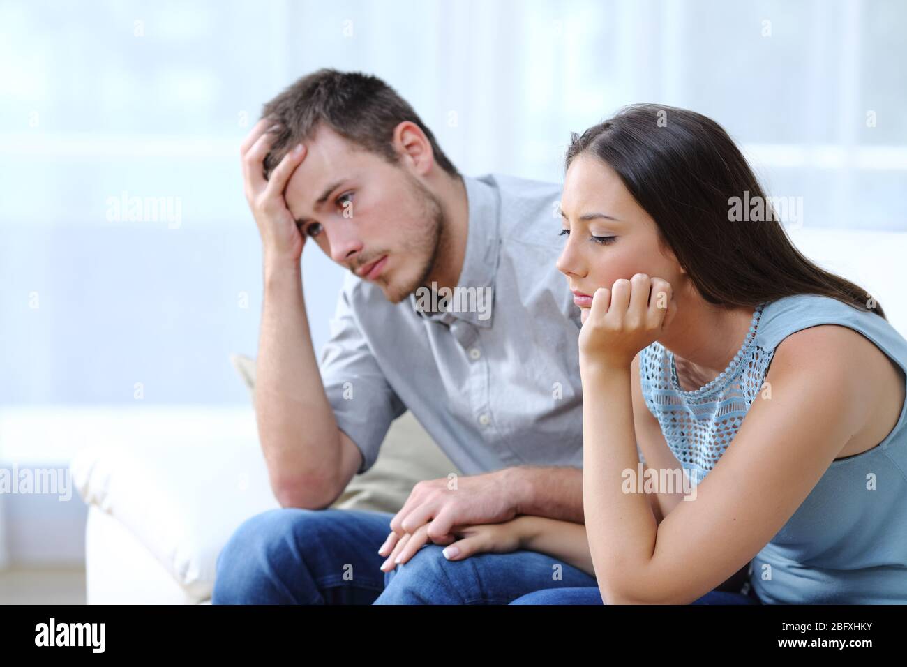 Triste coppia preoccupata lamentandosi insieme tenendo le mani su un divano a casa Foto Stock