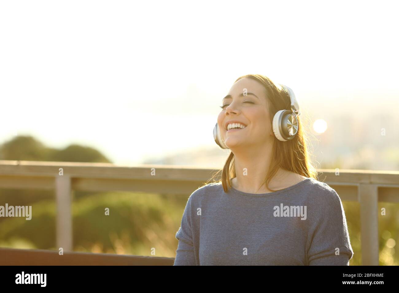 ragazza sicura e felice che ascolta la musica con le cuffie al tramonto in un parco Foto Stock