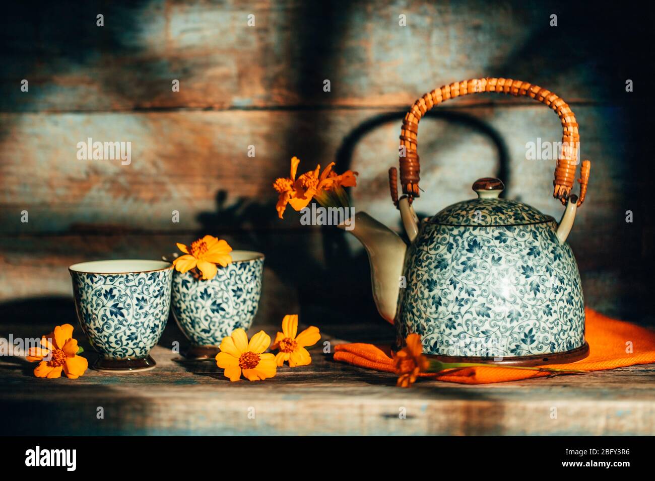 Stiil vita con i fiori di Chernobrivtsi in teiera vintage e tazze su sfondo rustico vecchio con luce del tramonto dalla finestra. Foto Stock