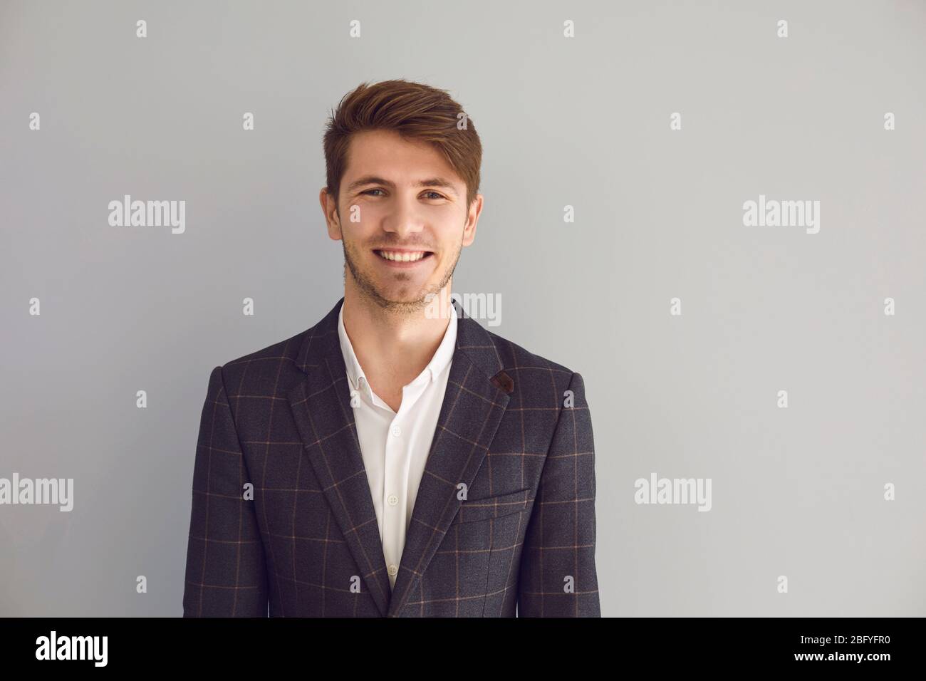 Giovane uomo in giacca sorridente ride allegro felice positivo su sfondo grigio. Foto Stock