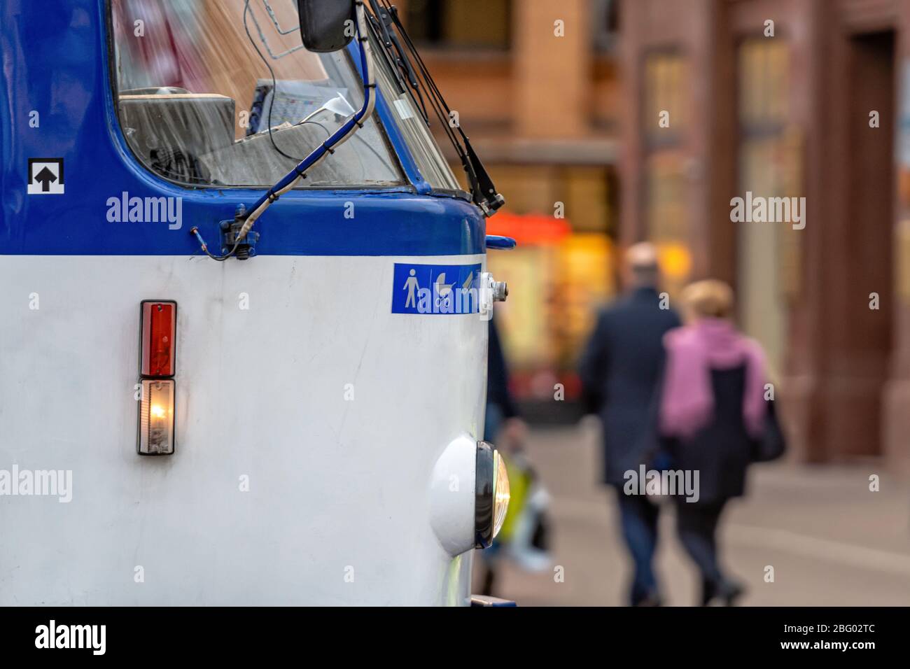 vista laterale da vicino della parte anteriore di un tram con una strada disfocalizzata con pedoni sullo sfondo Foto Stock