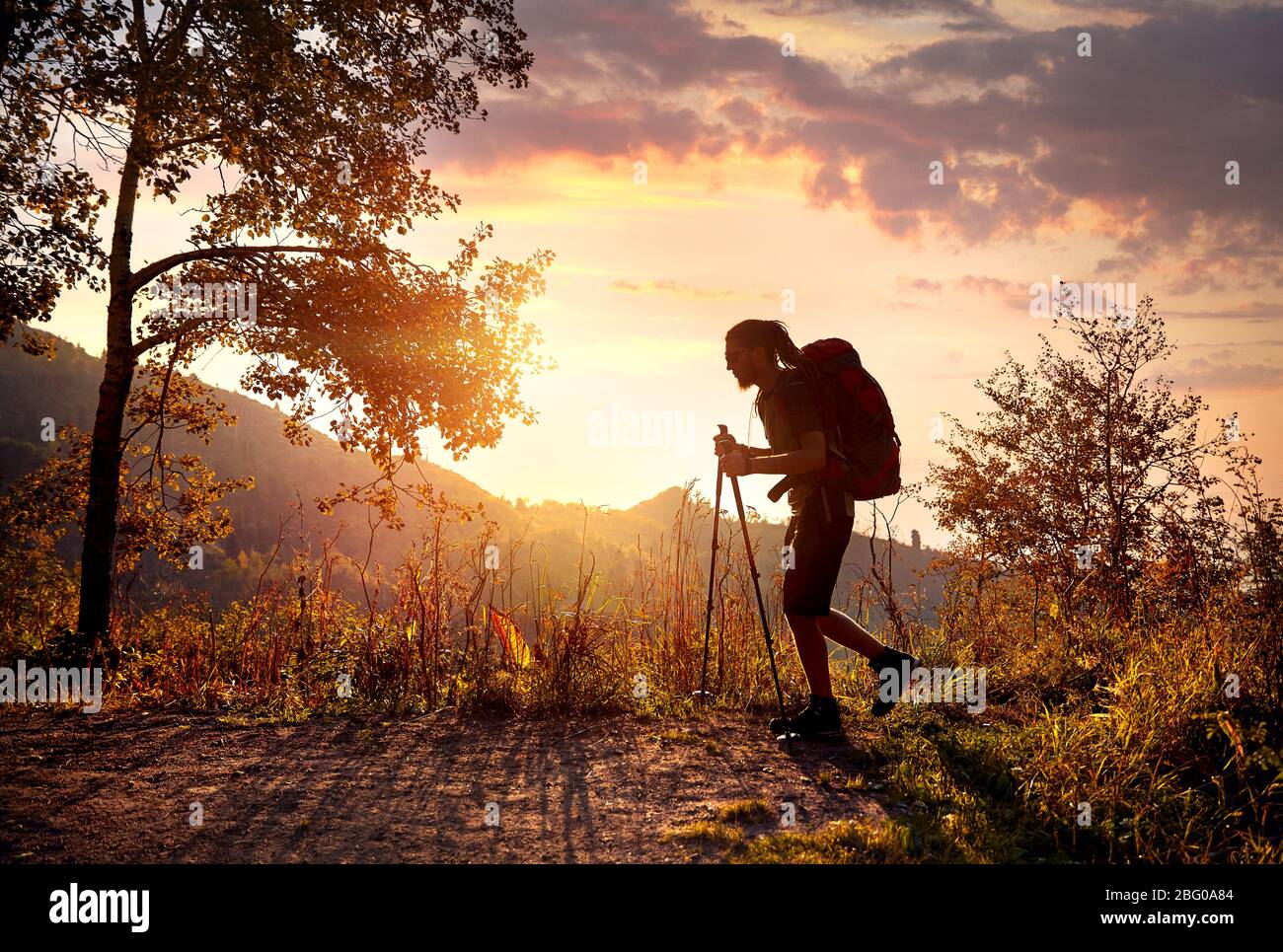 Uomo con dreadlocks e zaino in silhouette escursione in montagna al tramonto arancione sullo sfondo del cielo Foto Stock