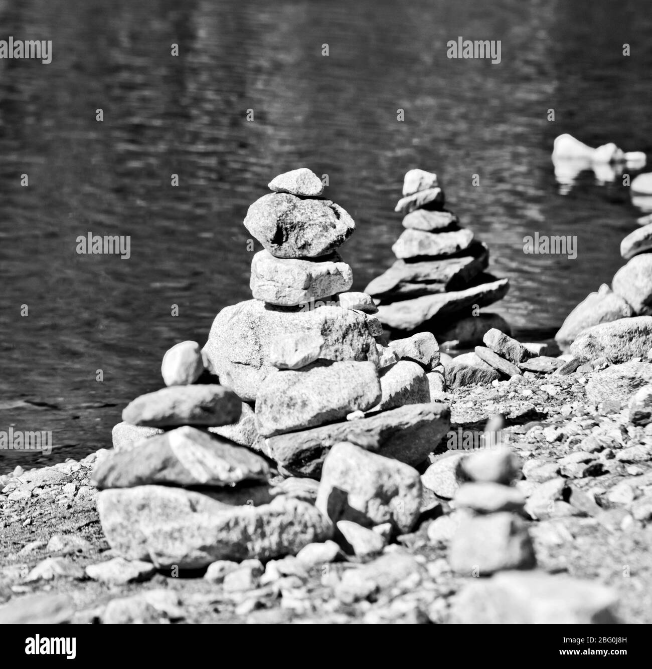 Piramidi di pietra, piccolo uomo, tumulo, ovoo, Inukshuk costruito per la vostra calma e tranquillità fatta vicino al lago o fiume di montagna in bianco e nero Foto Stock