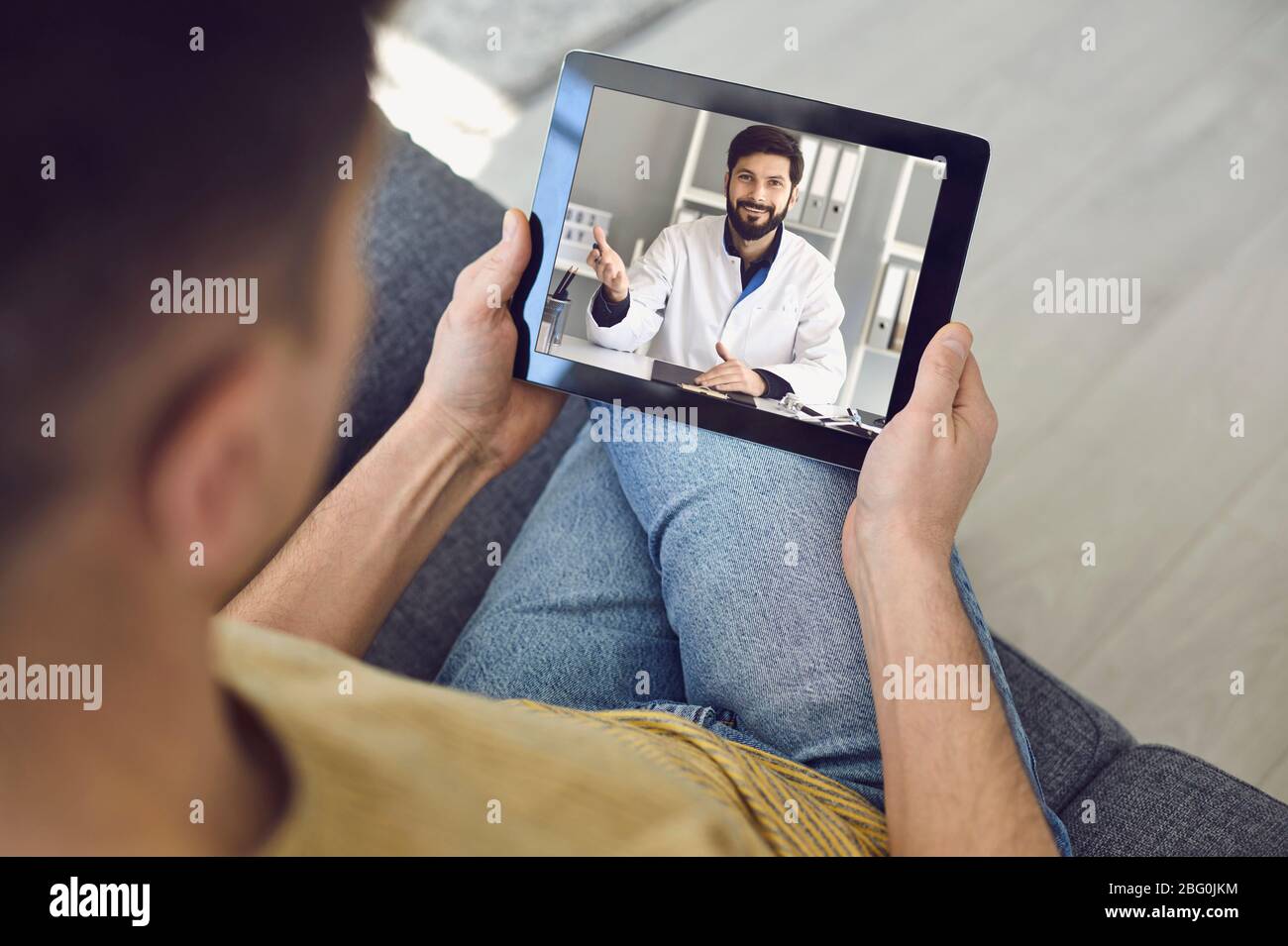 Consulenza medica online per i pazienti. La videochiamata del medico con il laptop parla con il paziente seduto sul divano a casa. Foto Stock