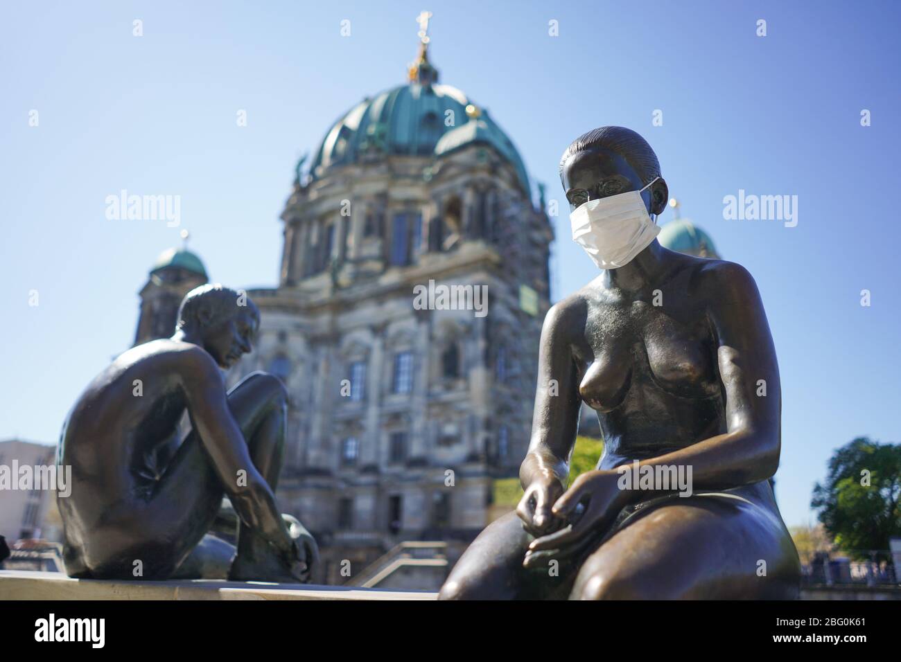 Berlino, Germania. 20 aprile 2020. ILLUSTRAZIONE - UNA figura della scultura 'tre ragazze e un ragazzo' dell'artista Wilfried Fritzenreiter sul fiume Sprea indossa una guardia della bocca. Credit: Jörg Carstensen/dpa/Alamy Live News Foto Stock