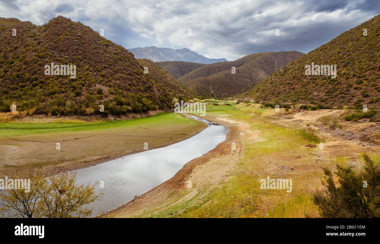 Una tranquilla scena autunnale di fiume tortuoso in una valle circondata da montagne e nuvole pesanti. Calitzdorp, Sudafrica Foto Stock