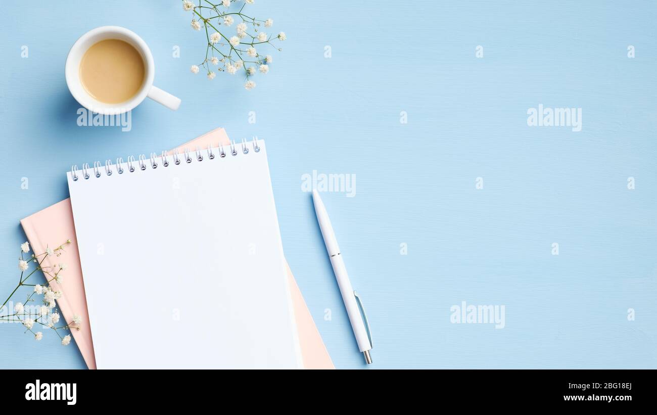 Piano di lavoro, vista dall'alto, femminile con blocco note vuoto, tazza di caffè, penna e fiori su sfondo blu. Scrivania da ufficio di stile minimalista, per lavoro Foto Stock