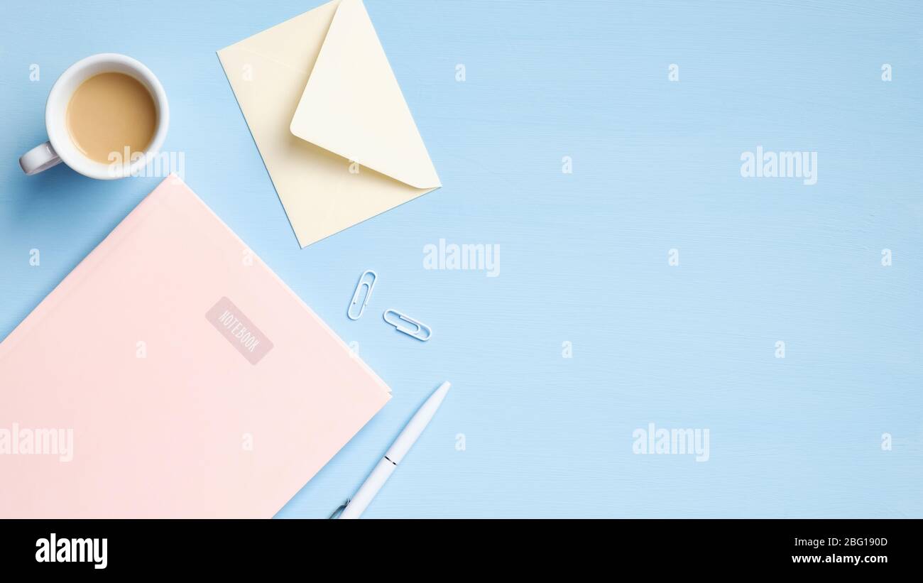 Piano, scrivania da ufficio con vista dall'alto. Spazio di lavoro femminile dallo stile minimale con notebook rosa, tazza di caffè, busta, penna su sfondo blu Foto Stock