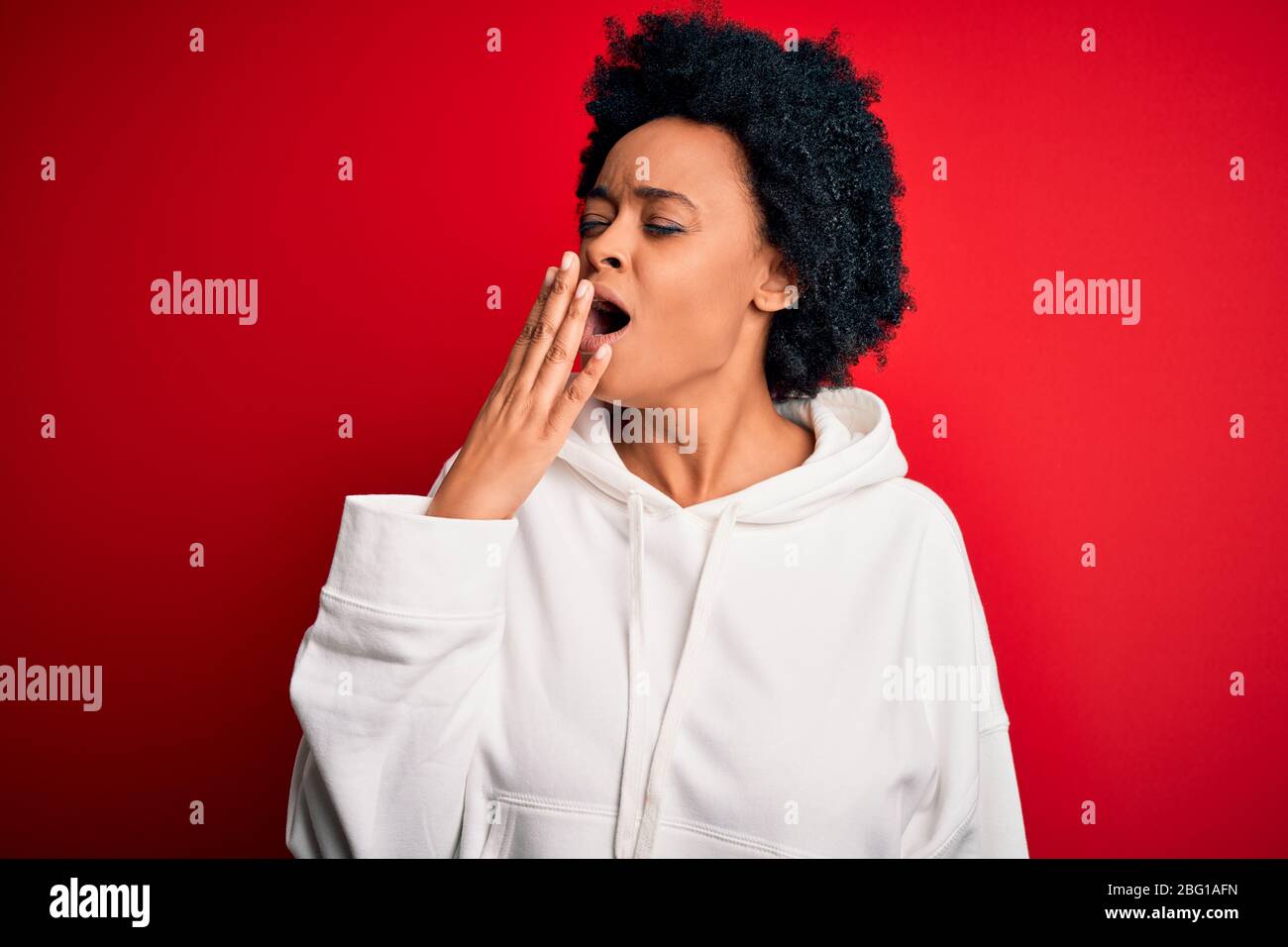 Giovane bella African American afro sportswoman con capelli ricci indossare sportswear annoiato yawning stanco coprendo bocca con mano. Inquieto e sleepi Foto Stock
