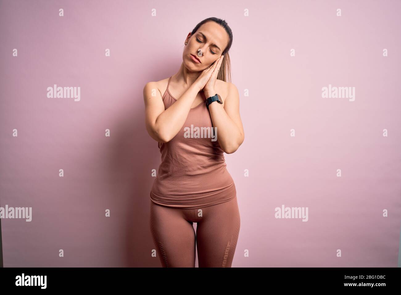 Giovane donna bionda fitness che indossa abiti sportivi su sfondo isolato rosa dormire stanco sognare e posare con le mani insieme mentre SM Foto Stock