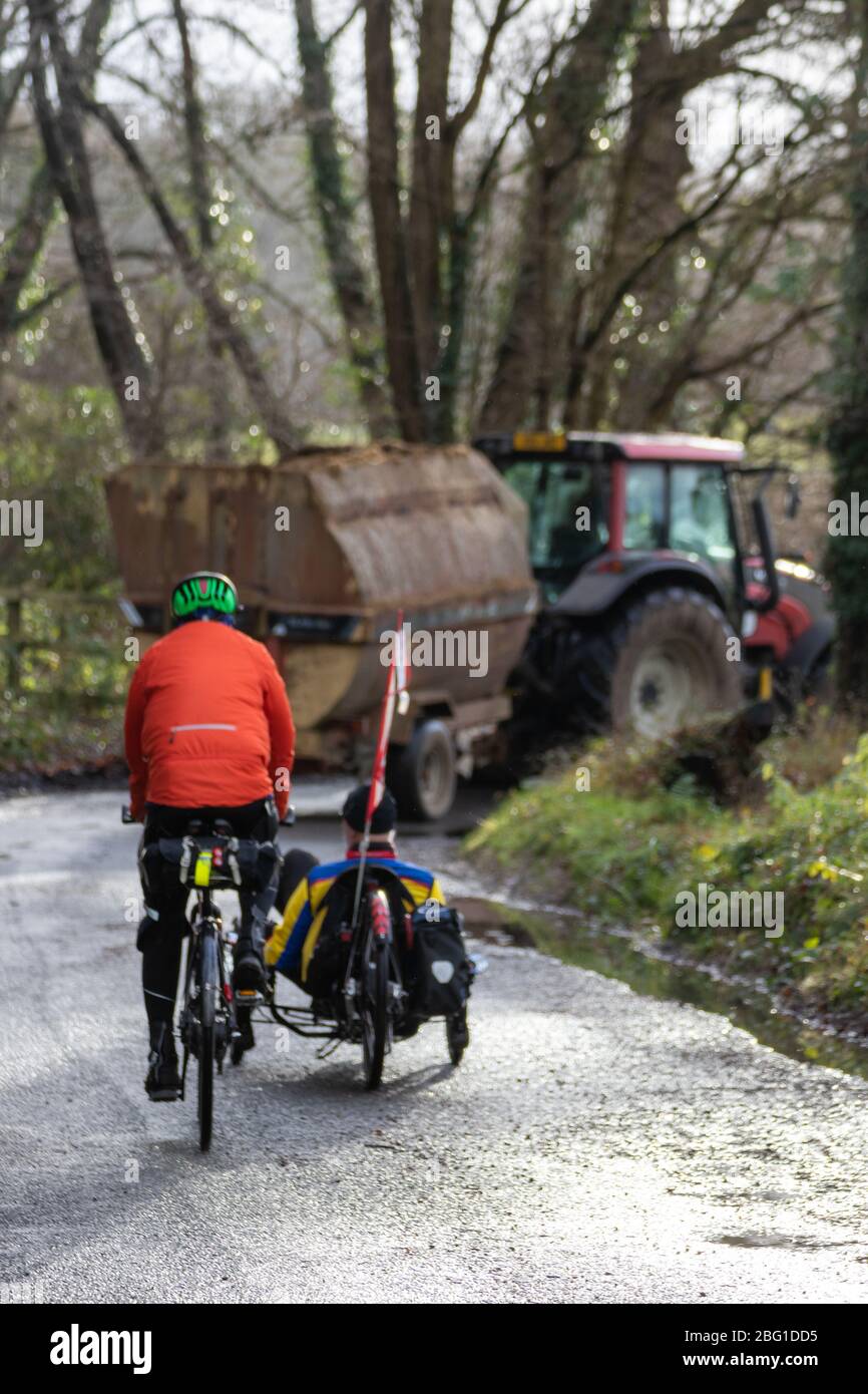 Ciclisti che guidano su corsie di campagna seguendo un trattore sullo sfondo Foto Stock