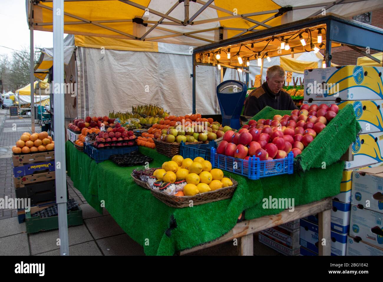 Un grocer che stenderà le scorte sulla sua bancarella di frutta e veg o di mercato Foto Stock