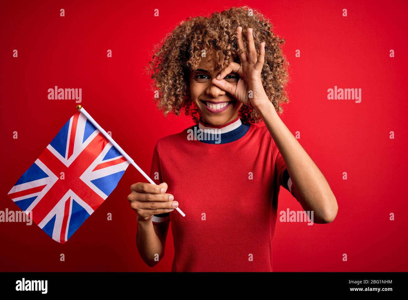 Giovane maledetta afro-americana che tiene la bandiera del regno unito celebrare il referendum sulla brexit con il volto felice sorridendo facendo un segno ok con mano sugli occhi guardando palpito Foto Stock