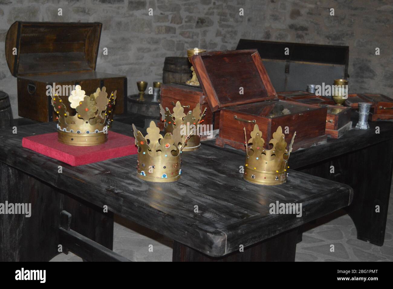 Un museo storico che mostra corone medievali dorate, calici e forzieri di tesori in legno aperti disposti su tavoli di legno scuro. Foto Stock