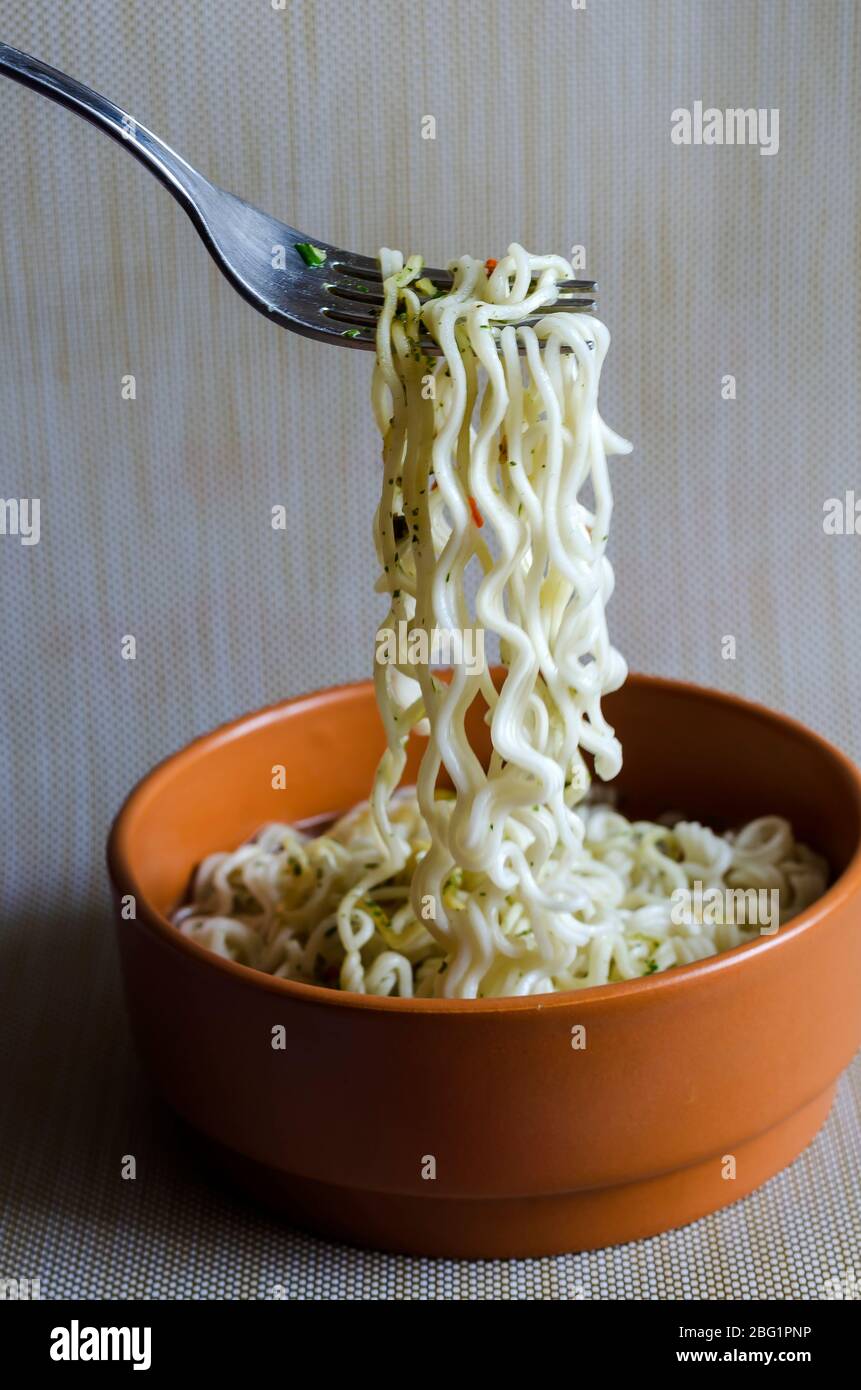 Ciotola con tagliatelle istantanee. Ciotola di argilla marrone con spaghetti lunghi e spezie. Spaghetti appesi su una forcella. Messa a fuoco selettiva. Foto Stock