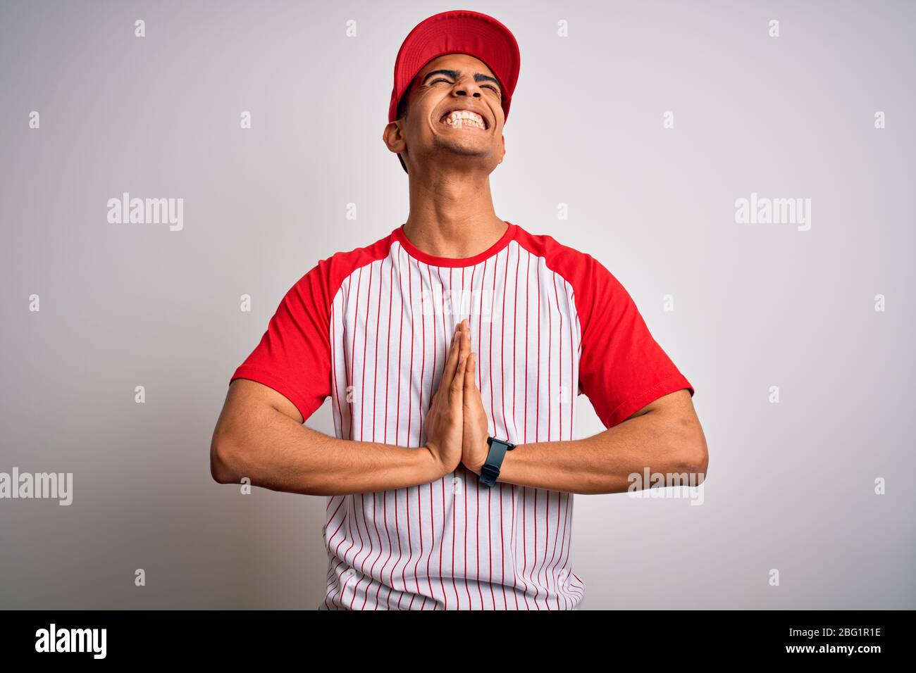 Giovane sportivo afro-americano con t-shirt e cappello a righe da baseball,  mendicante e pregante con le mani insieme all'espressione della speranza  sulla fac Foto stock - Alamy