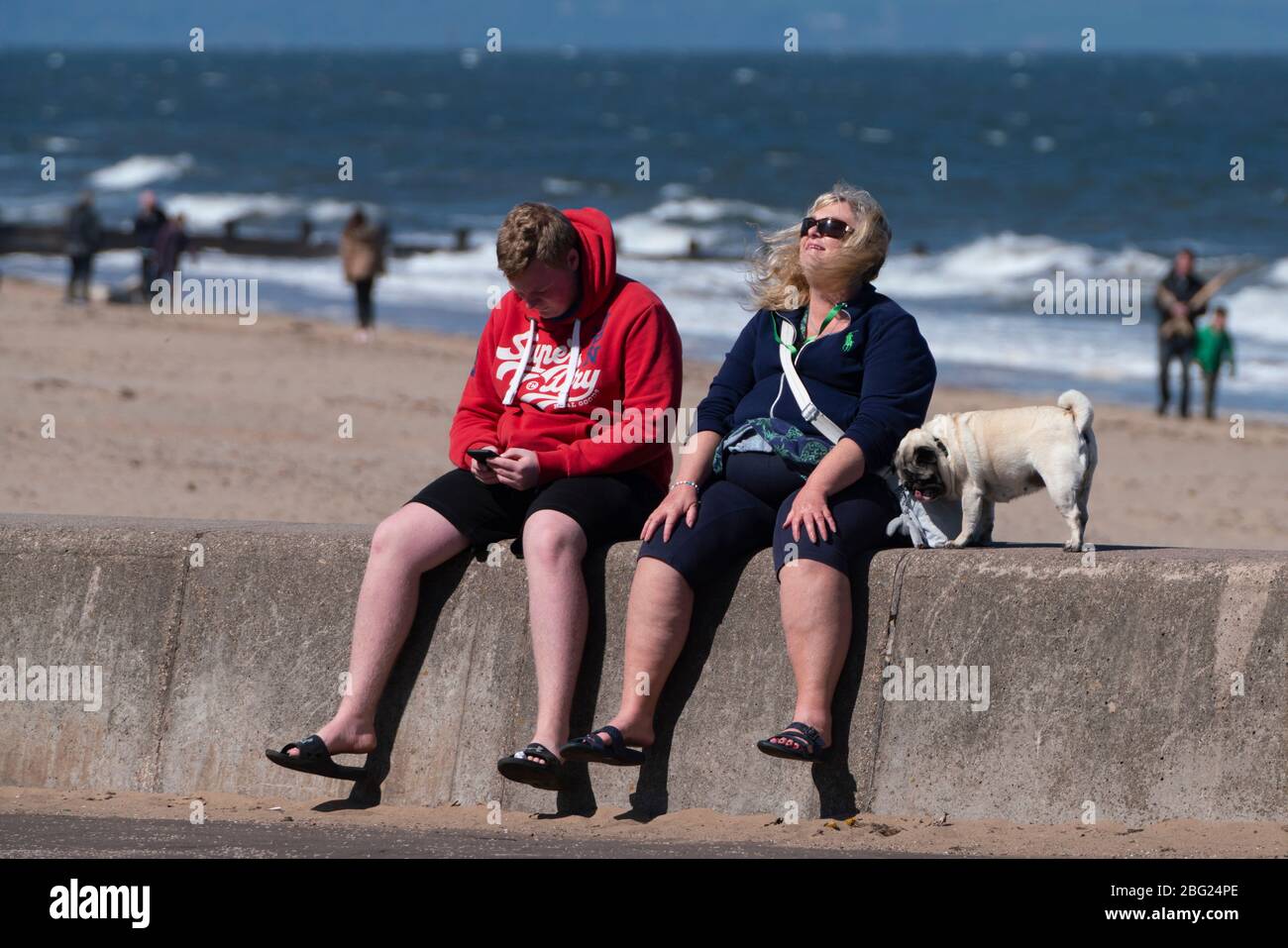 Spiaggia di Portobello e passeggiata vicino Edimburgo durante il blocco di Coronavirus il 19 aprile 2020. Coppia con cane seduto sul muro di mare. Foto Stock