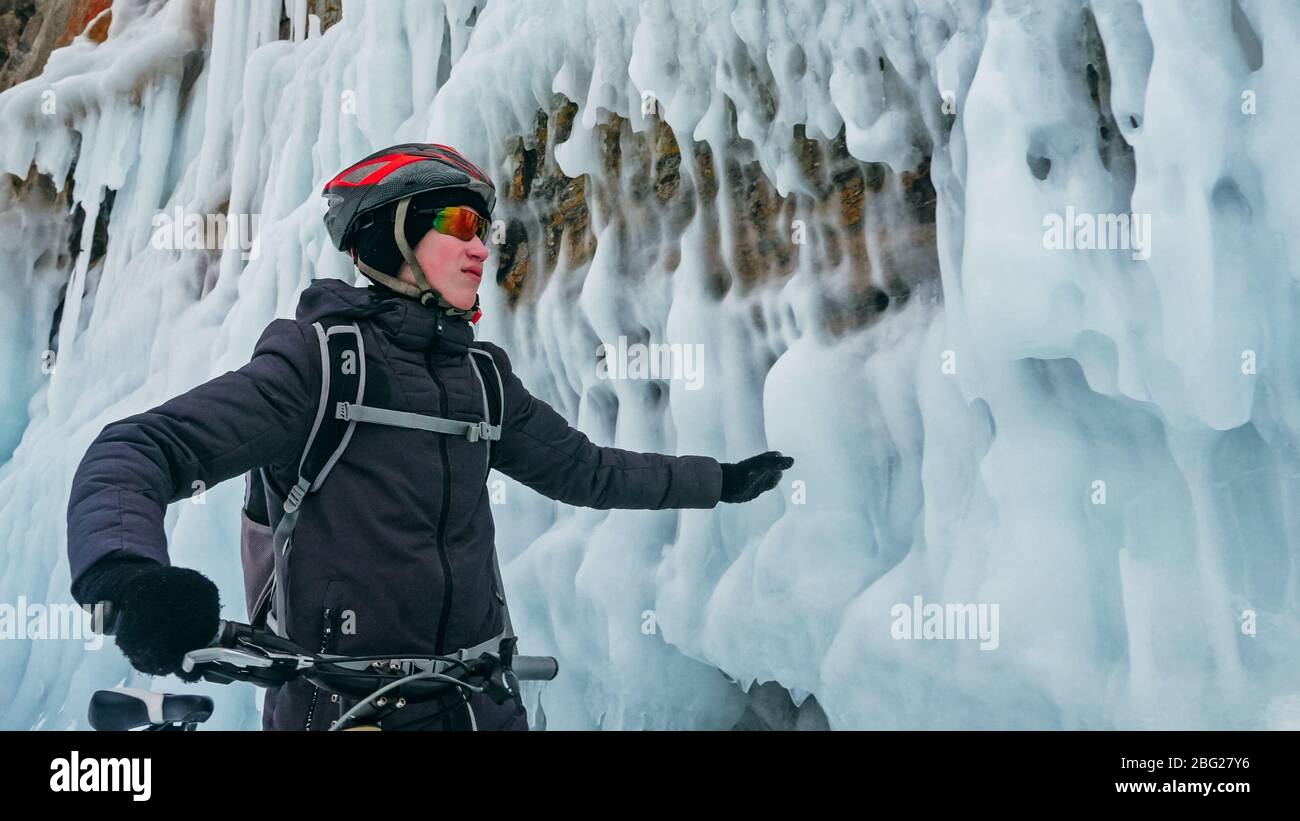 L'uomo sta pedalando vicino alla grotta di ghiaccio. Roccia con grotte di ghiaccio icicll Foto Stock