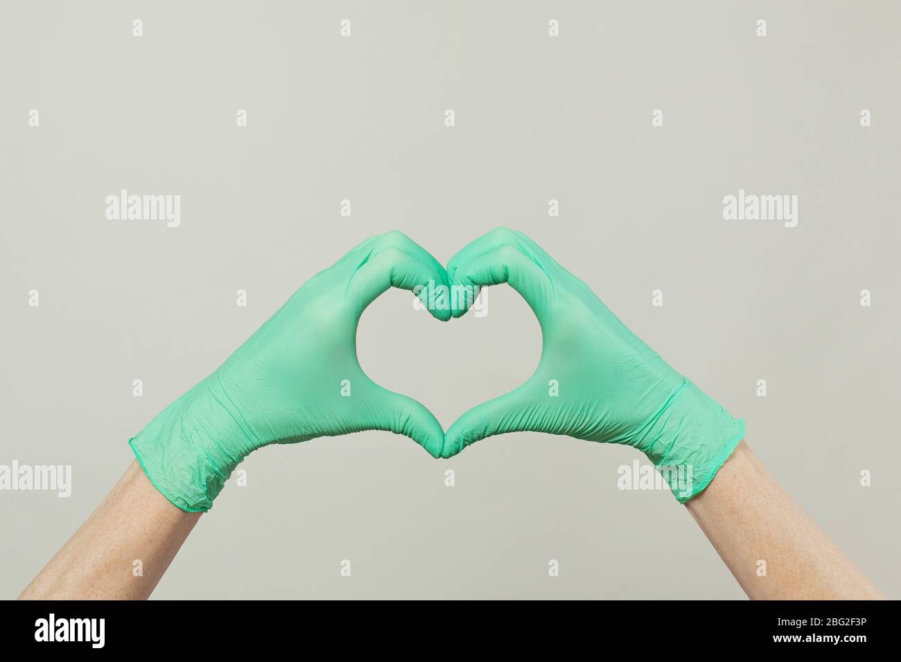 Mani in guanti verdi medico fare cuore su sfondo grigio Foto Stock