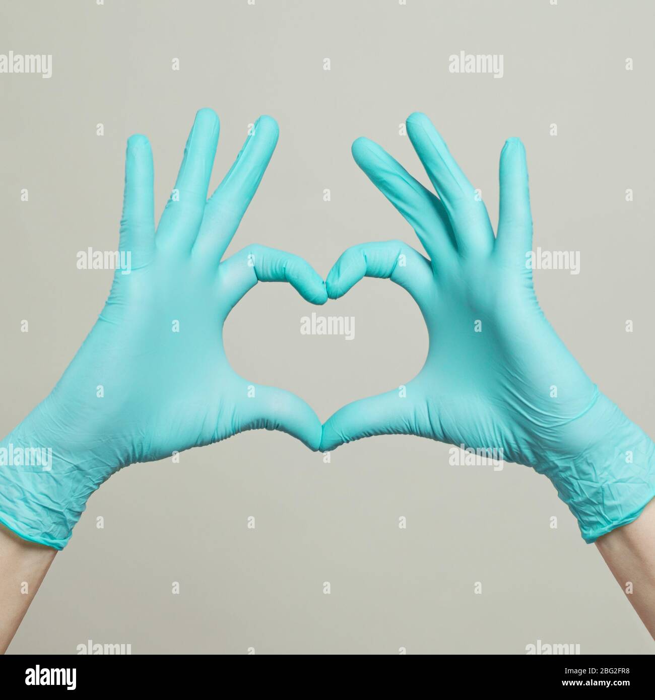 Cuore dalle mani in guanti blu medico su sfondo grigio. Concetto di assistenza medica Foto Stock