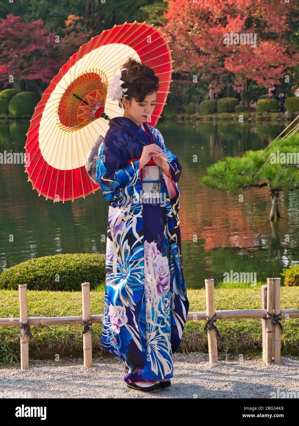 Una giovane donna in colorato abito nazionale posa per fotografie in un parco pubblico a Kanazawa, Giappone, in una giornata di sole, autunno. Foto Stock