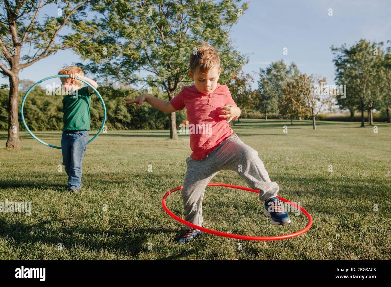 Due divertenti ragazzi caucasici prescolare che giocano con un cerchio di hoola nel parco esterno. Attività sportive per bambini. Stile di vita felice infanzia. Estate stagionale all'aperto Foto Stock