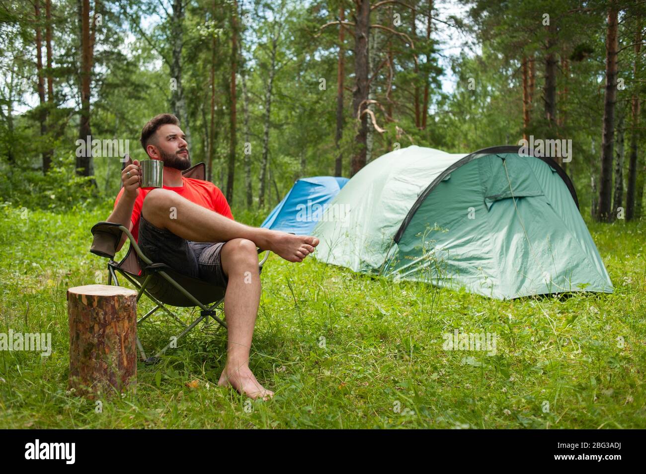 Godersi la vita. Il giovane in natura beve il tè, sullo sfondo di un campeggio. Relax, vacanze, stile di vita Foto Stock