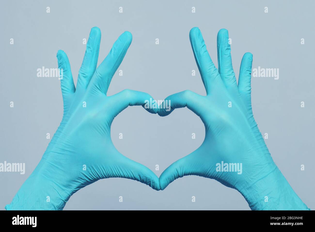 Mani in guanti blu medico facendo cuore su sfondo grigio. Concetto di assistenza medica Foto Stock