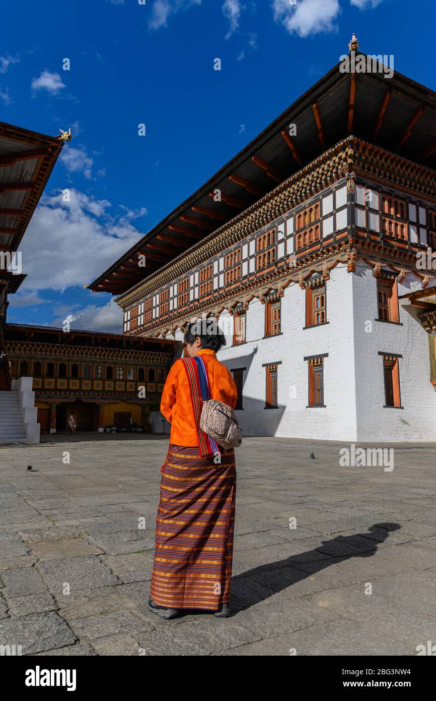 Vista posteriore di una donna in abiti tradizionali in piedi fuori Tashichho Dzong, Thimphu, Bhutan Foto Stock