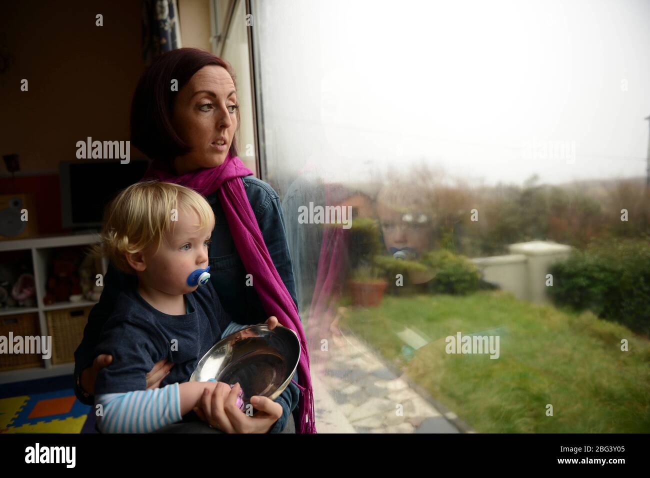 Una giovane madre che soffre di depressione post-natale siede ad una finestra con il suo bambino Foto Stock