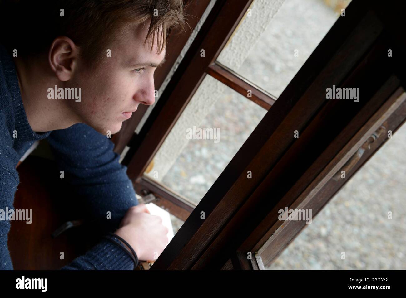 Un giovane uomo che soffre di depressione guarda fuori una finestra che si chiede come affrontare il giorno che ci attende. Foto Stock