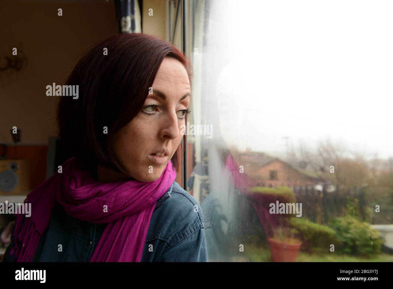 Una giovane madre che soffre di depressione siede in una finestra Foto Stock