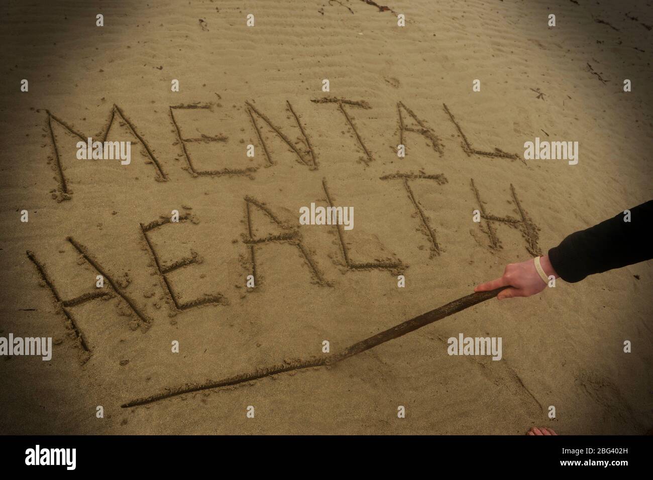Un giovane che soffre di depressione scrive le parole salute mentale nella sabbia Foto Stock