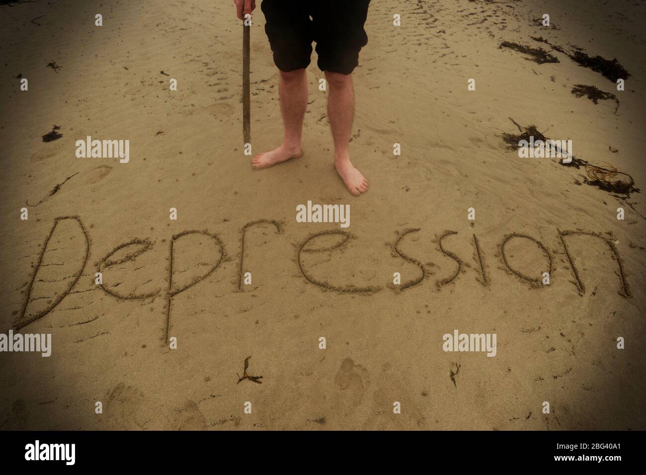Un giovane che soffre di depressione scrive la parola nella sabbia. Foto Stock