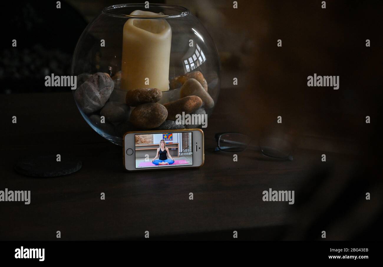 Una donna matura di mezza età che fa la mente di rilassamento ed esercitazioni di respirazione a casa guardando una lezione sul suo smartphone Foto Stock