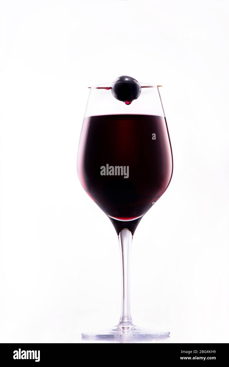Vino sgocciolante dall'uva rossa sopra un bicchiere di vino rosso di classe; immagine concettuale del sacrificio Foto Stock