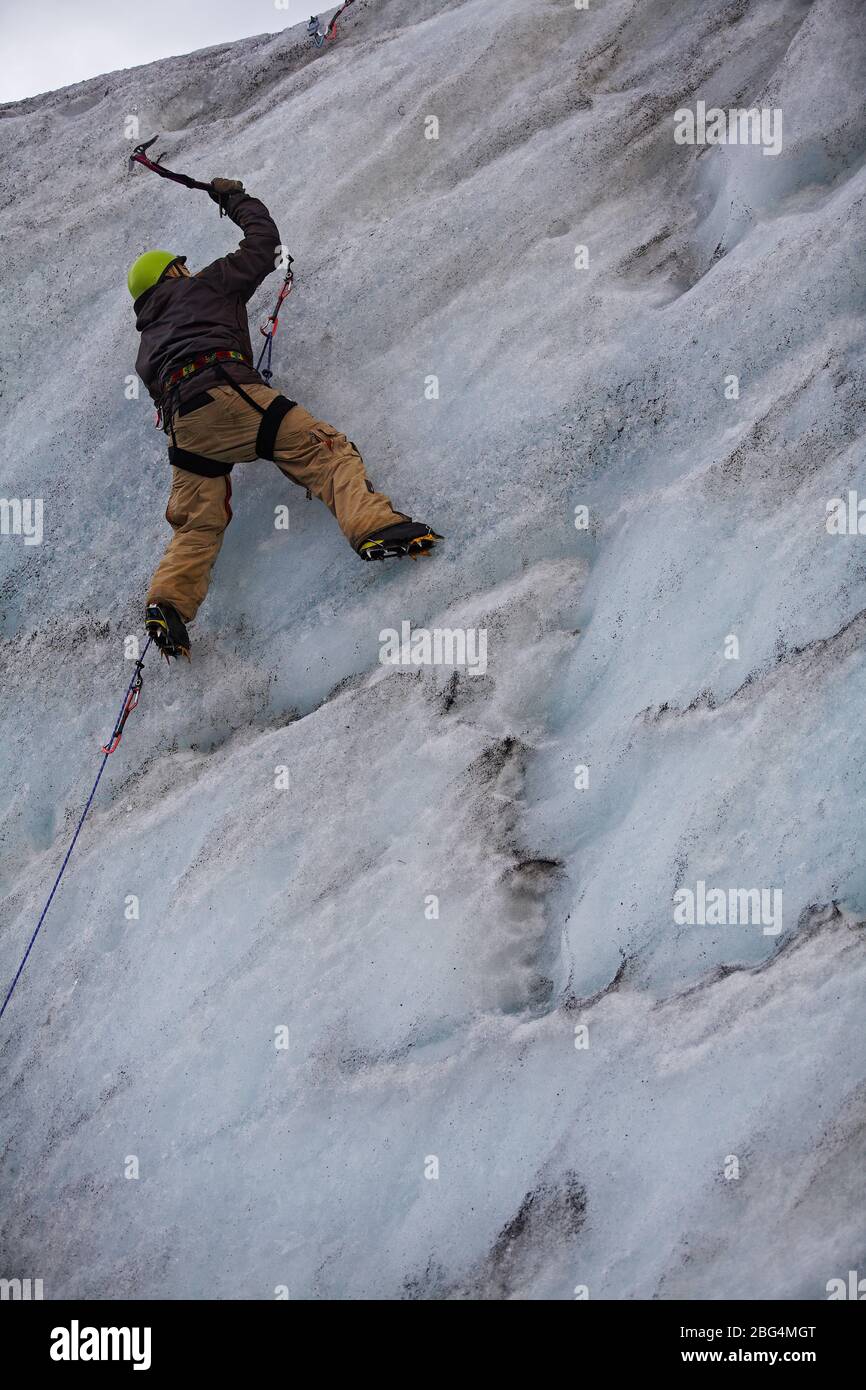 Giovane uomo che arrampica il muro di ghiaccio al ghiacciaio Solheimajokull in Islanda Foto Stock