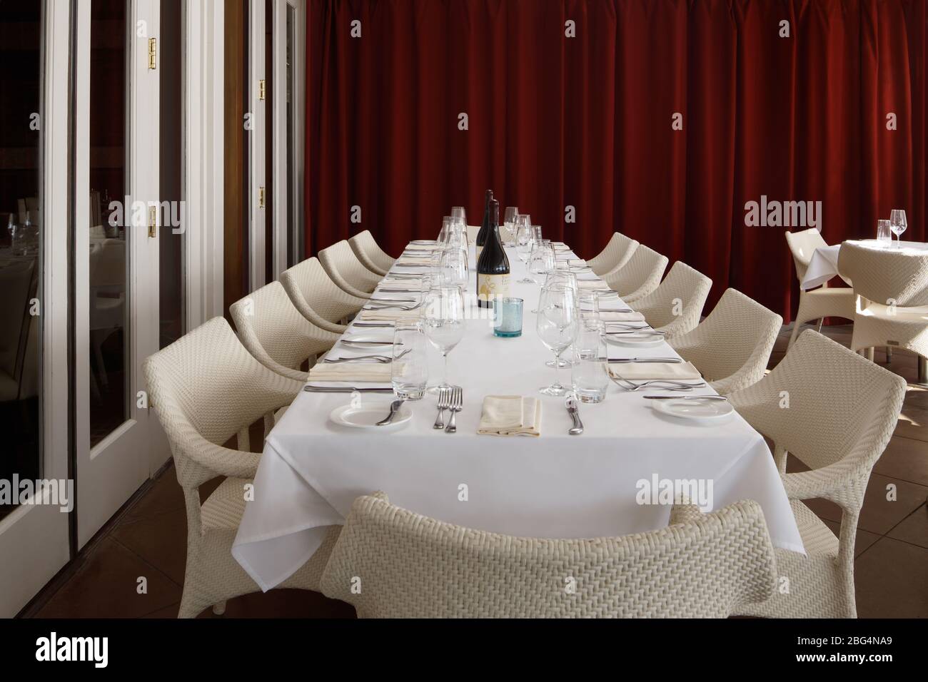 Un tavolo bianco con biancheria bianca e sedie bianche accanto al muro rosso Foto Stock