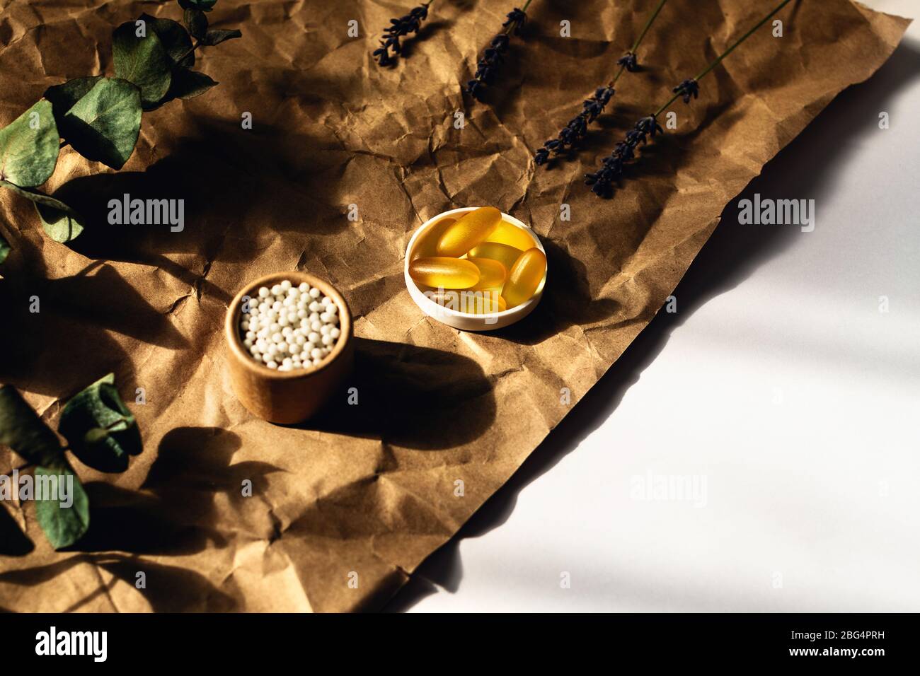 Piatto con capsule di olio di pesce e palle omeopatiche adagiate su carta da imballaggio stropicciata. Circondato da rametti di eucalipto e lavanda. Foto Stock