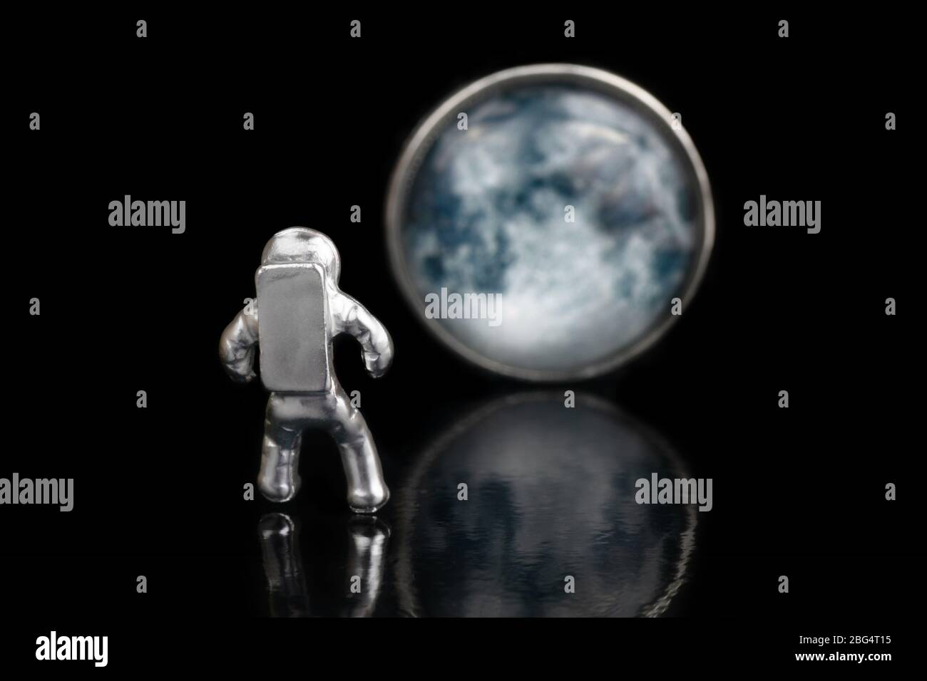 Uomo spaziale in acciaio miniaturizzato che guarda la Luna. Primo piano, isolato su nero, fuoco selettivo. Foto Stock