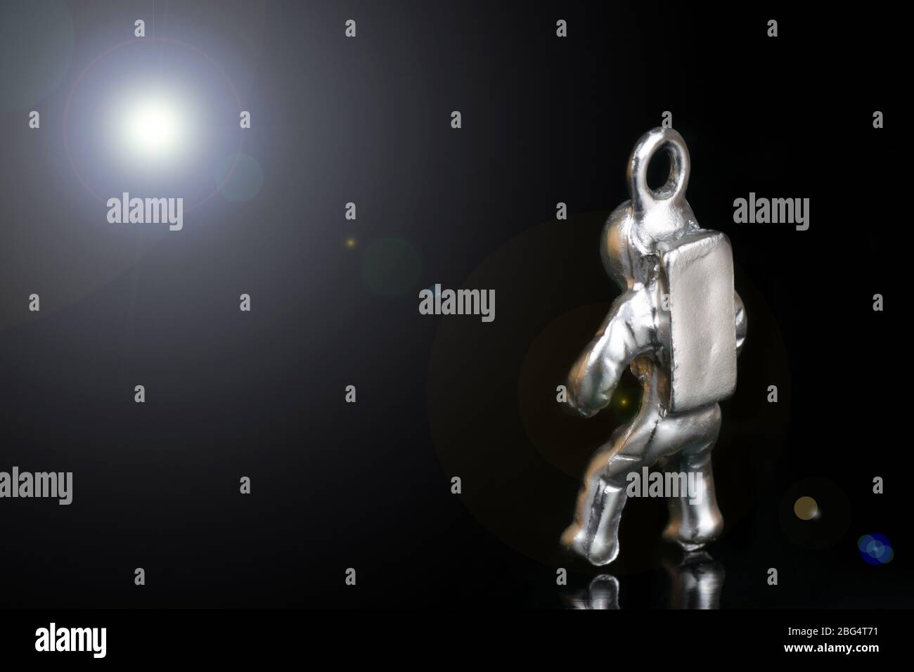 Minuscola statuina d'acciaio di un astronauta che guarda la luce di una stella lontana. Primo piano, isolato su nero, con lente svasata. Foto Stock