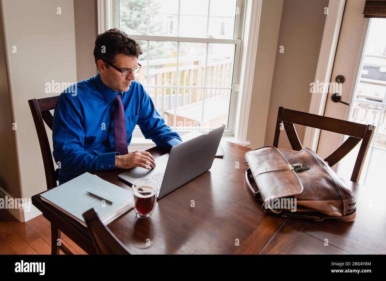 Uomo in camicia e cravatta che lavora da casa usando il computer al tavolo da pranzo. Foto Stock