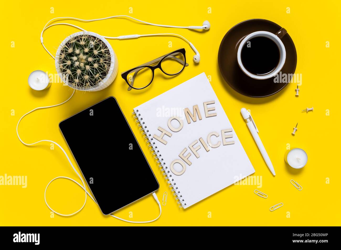 Disposizione piatta di spazio di lavoro moderno con tablet, auricolari, tazza da caffè, blocco note, penna, occhiali e cactus. Lettere che dicono Ufficio domestico. Vista dall'alto su giallo b Foto Stock