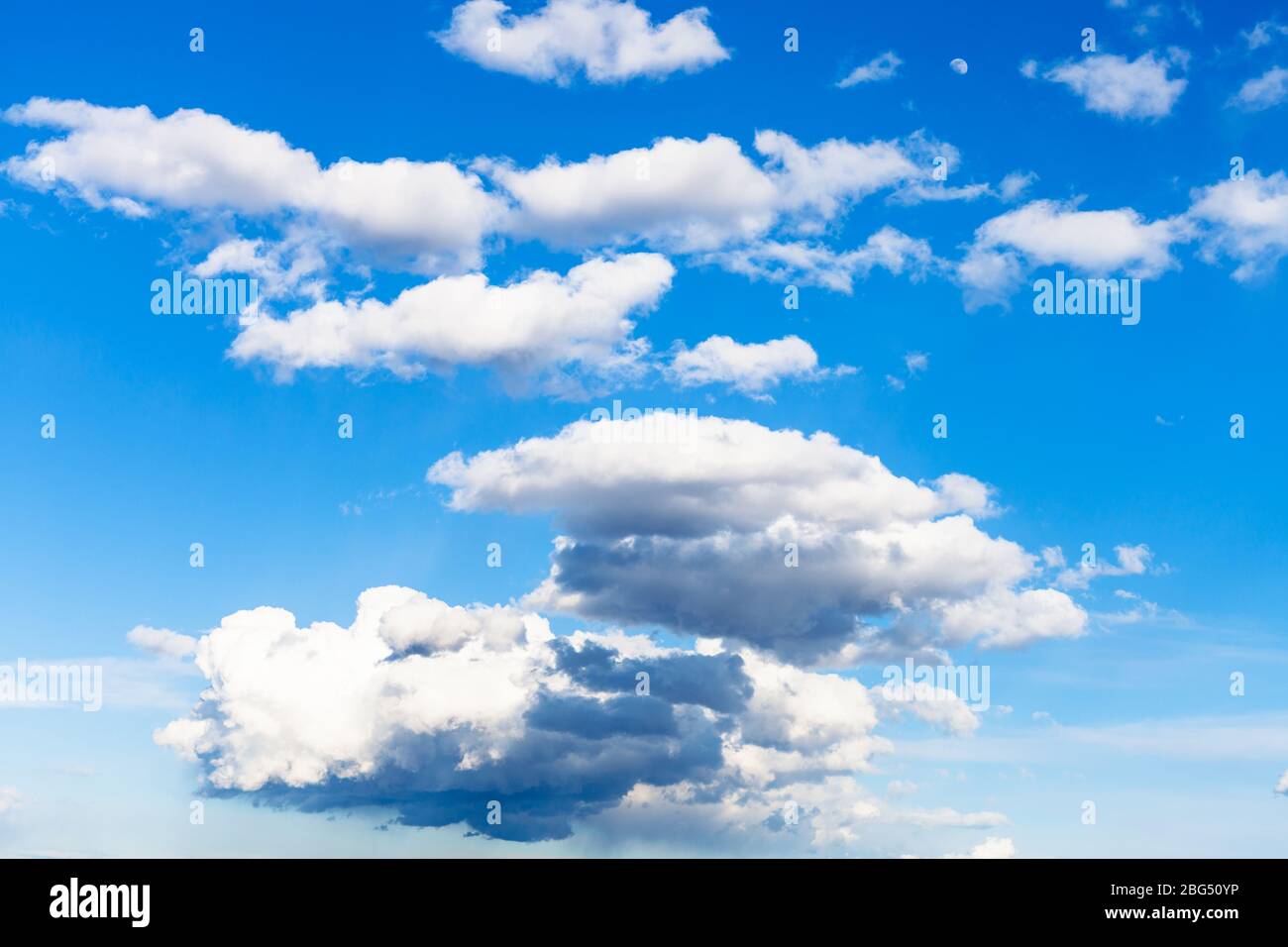 Poche nuvole basse e scure e molte nuvole bianche nel cielo blu il giorno di marzo Foto Stock